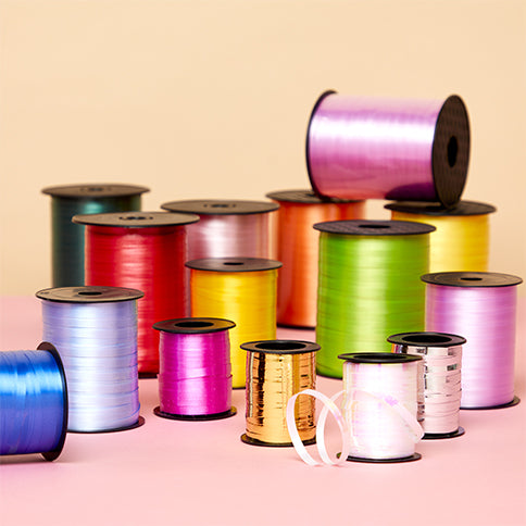 Colourful balloon ribbon spools arranged on a pastel party backdrop.