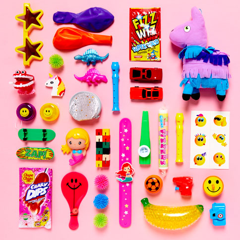 Colourful party toys and small surprises styled on a bright pink backdrop.