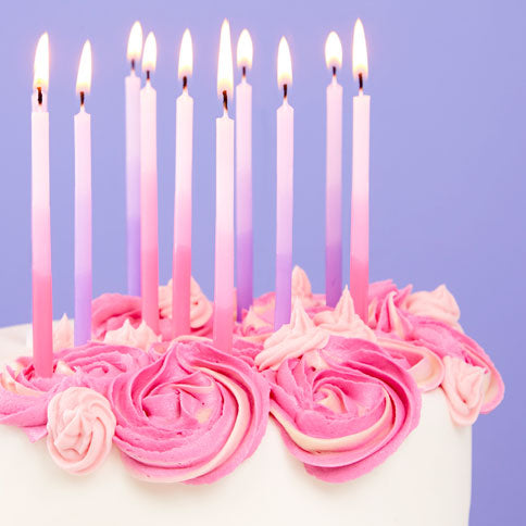 Lit pink birthday candles on a decorated cake, styled against a purple party backdrop.
