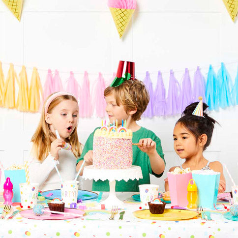 Children celebrating a birthday with a cake, pastel tassel decorations and colourful party tableware.