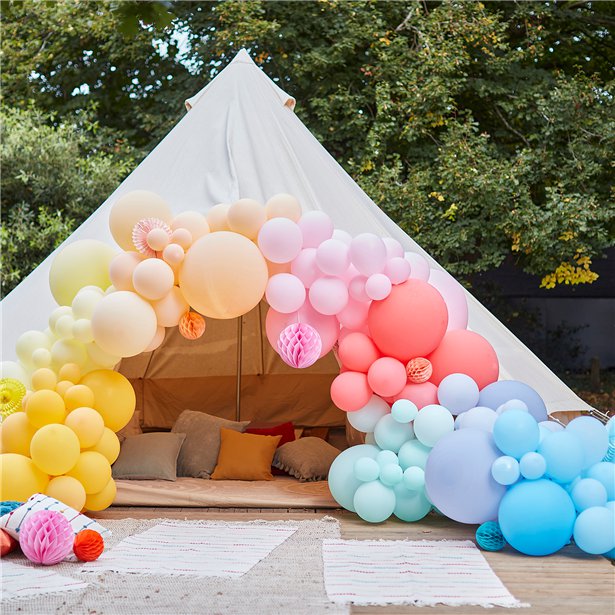 Finished Brights & Fans rainbow balloon arch with colourful paper decorations framing a white party tent.