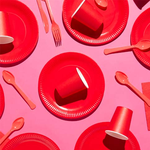 Red party plates, napkins and cutlery styled on a pink party backdrop.