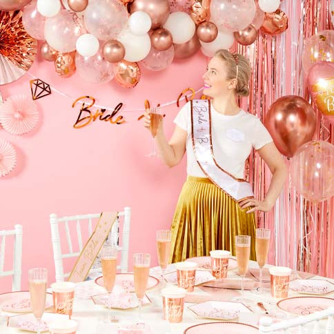 A bride to be enjoying a celebration beside a styled balloon and flower backdrop.